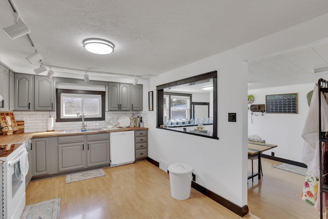 kitchen featuring white appliances, light wood-style flooring, gray cabinets, a sink, and tasteful backsplash