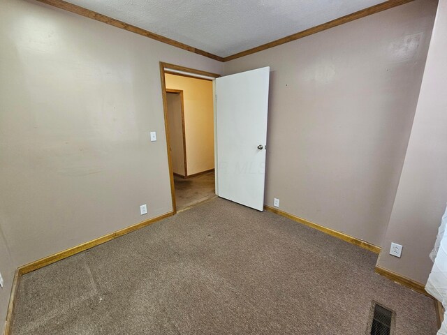 carpeted spare room with visible vents, a textured ceiling, crown molding, and baseboards