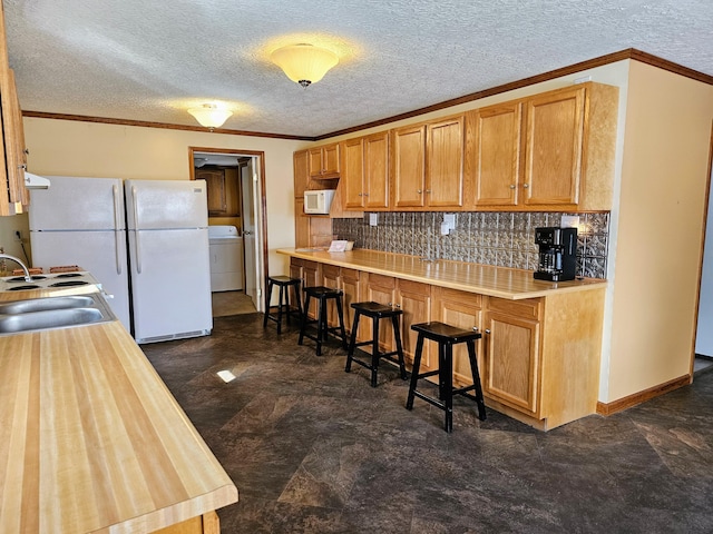 kitchen with crown molding, light countertops, washer / dryer, white appliances, and a sink