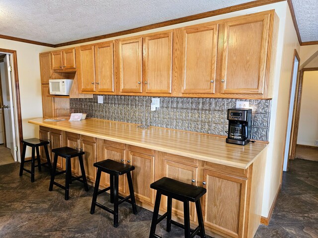 kitchen featuring white microwave, a textured ceiling, crown molding, a kitchen breakfast bar, and tasteful backsplash