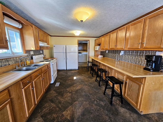 kitchen with under cabinet range hood, white appliances, backsplash, and a sink