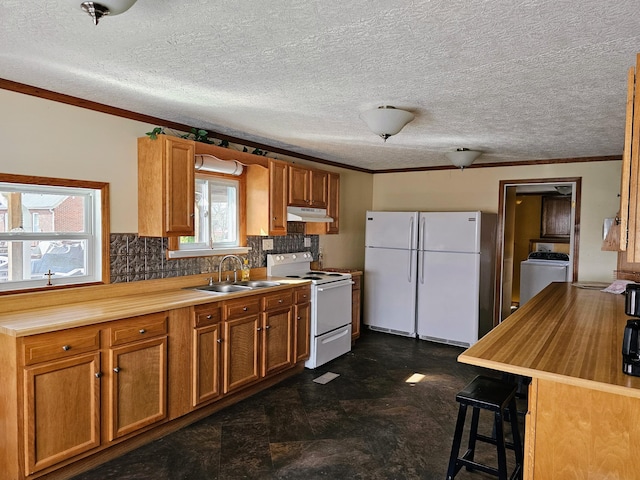 kitchen featuring crown molding, under cabinet range hood, white appliances, washer / clothes dryer, and a sink