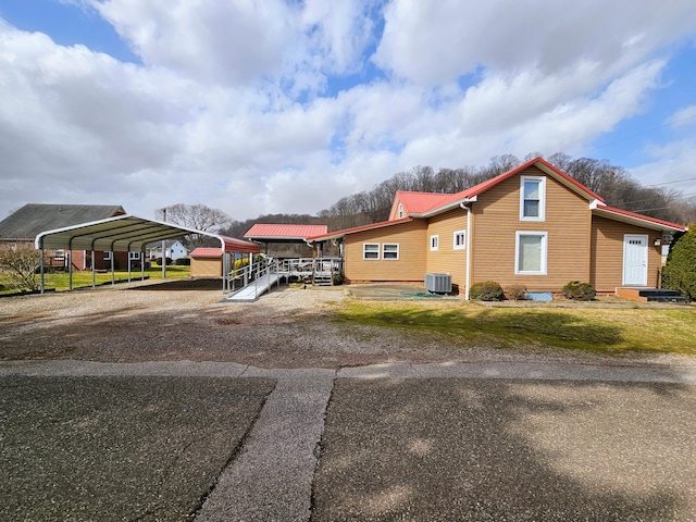 view of side of property with central air condition unit, a carport, metal roof, and a yard