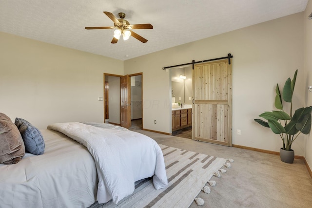bedroom with connected bathroom, a barn door, a walk in closet, light carpet, and baseboards