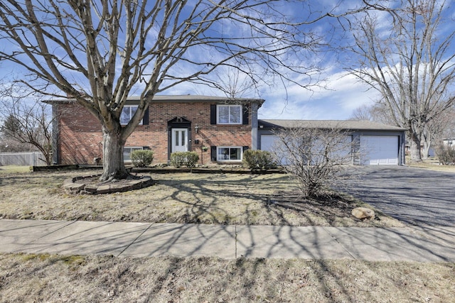 bi-level home featuring brick siding, driveway, a garage, and fence