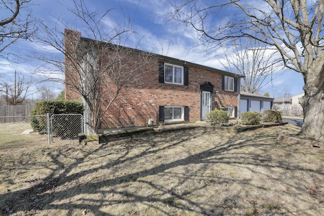 bi-level home featuring brick siding, a garage, a gate, and fence