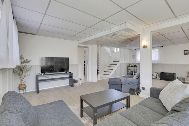 living area featuring a drop ceiling, stairs, and carpet