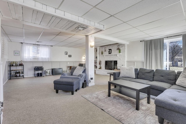 carpeted living room featuring a drop ceiling and a brick fireplace