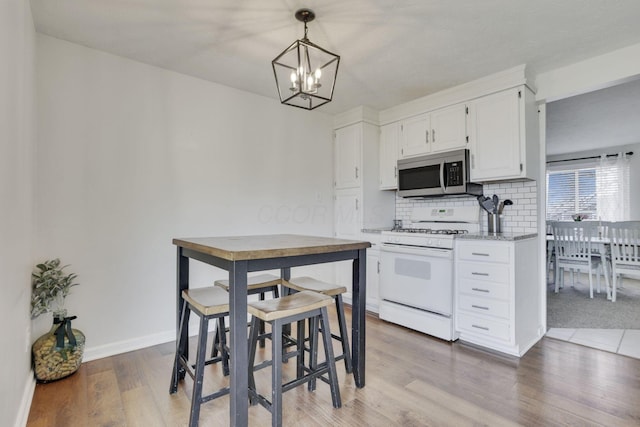 kitchen featuring tasteful backsplash, stainless steel microwave, white range with gas cooktop, light wood-style floors, and white cabinets