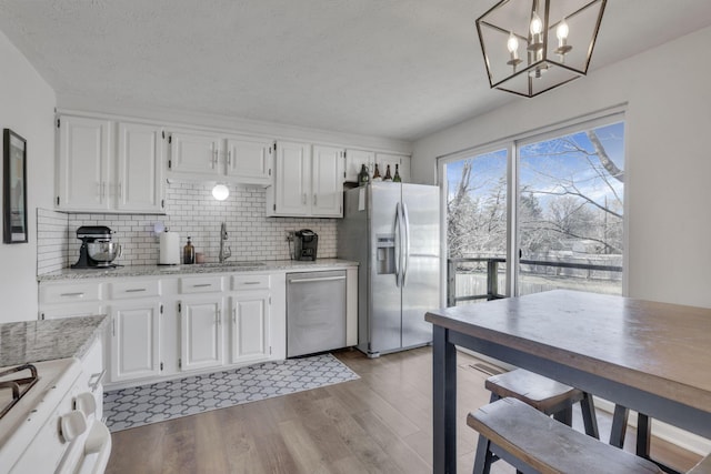 kitchen featuring white cabinets, light wood finished floors, tasteful backsplash, and appliances with stainless steel finishes