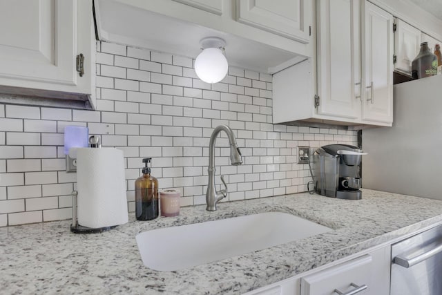 kitchen with a sink, light stone counters, tasteful backsplash, and white cabinets