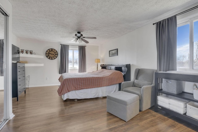 bedroom with ceiling fan, baseboards, a textured ceiling, and wood finished floors