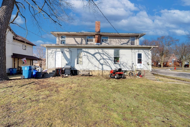 back of house with entry steps, a lawn, and a chimney