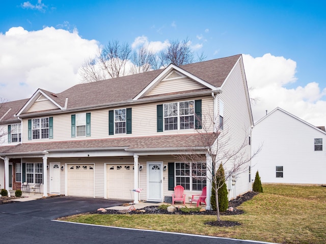 townhome / multi-family property with a front yard, an attached garage, driveway, and roof with shingles