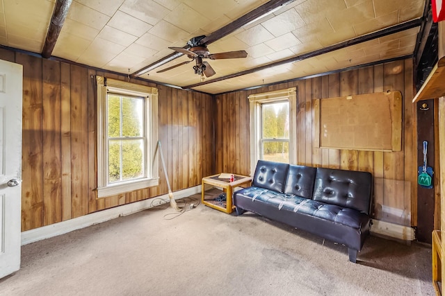 carpeted living room featuring baseboards, wooden walls, and a ceiling fan