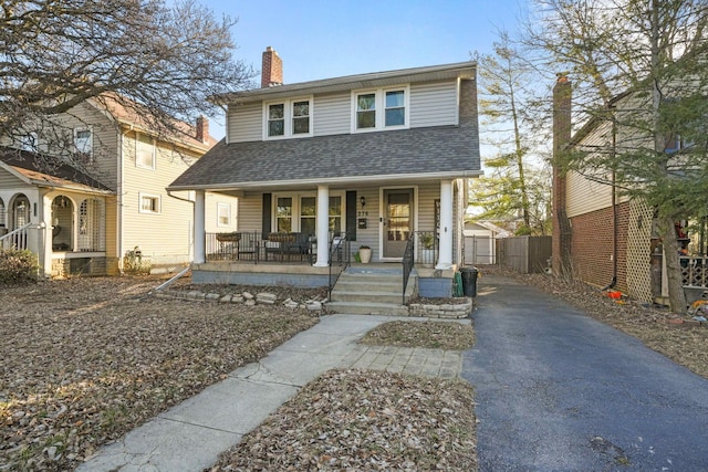 view of front of property with roof with shingles, a porch, a chimney, and fence