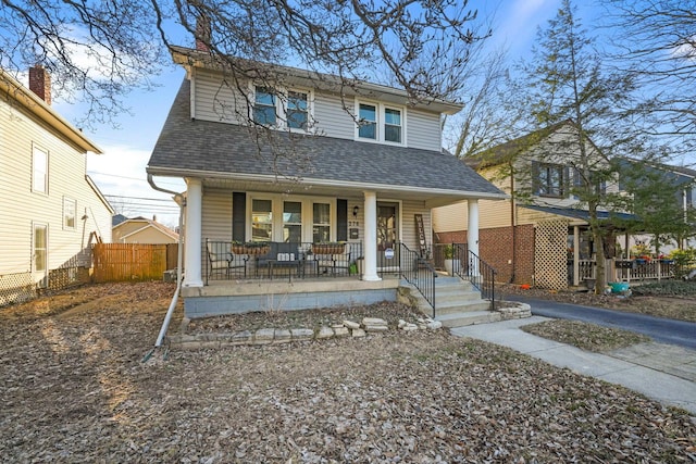 view of front facade with covered porch, a shingled roof, and fence