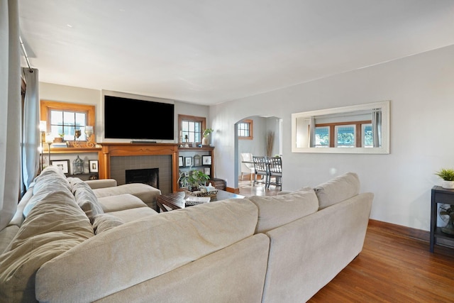 living area with a brick fireplace, wood finished floors, arched walkways, and baseboards