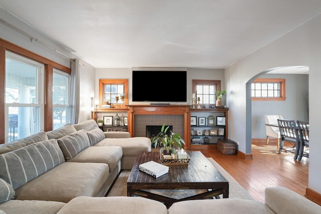 living area with wood finished floors, a fireplace, arched walkways, and baseboards