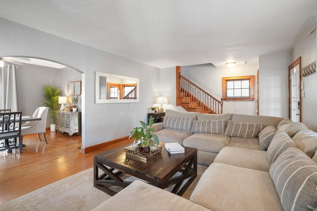 living area featuring arched walkways, stairway, a healthy amount of sunlight, and wood finished floors