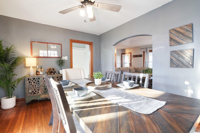 dining area with wood finished floors, arched walkways, and ceiling fan