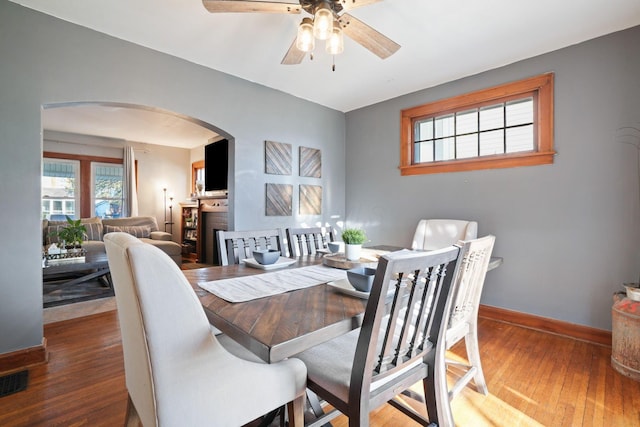 dining area with a ceiling fan, visible vents, wood finished floors, baseboards, and arched walkways