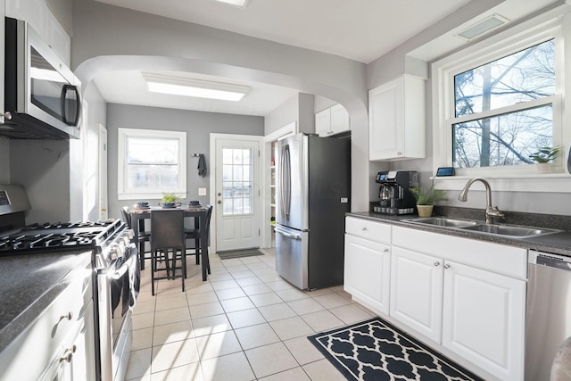 kitchen featuring a sink, dark countertops, stainless steel appliances, arched walkways, and light tile patterned floors