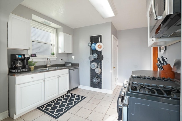 kitchen featuring light tile patterned floors, baseboards, a sink, stainless steel appliances, and white cabinetry