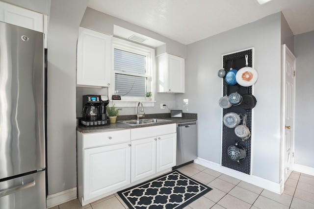 kitchen with a sink, dark countertops, appliances with stainless steel finishes, white cabinets, and light tile patterned floors