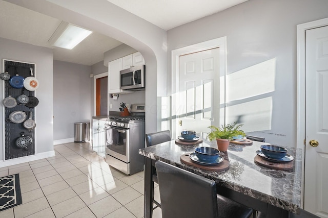 kitchen featuring dark countertops, arched walkways, appliances with stainless steel finishes, white cabinets, and light tile patterned floors