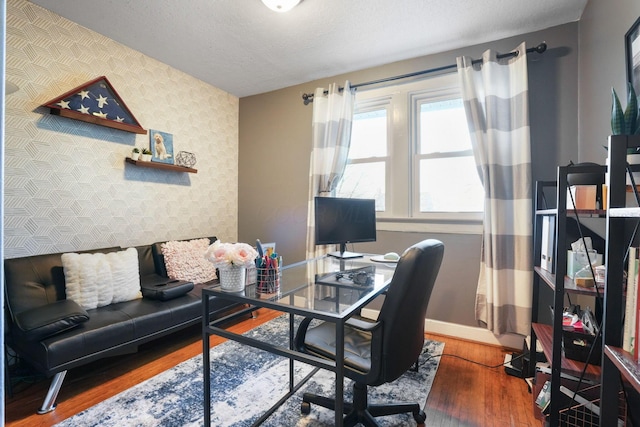 office area featuring a textured ceiling, wood finished floors, wallpapered walls, baseboards, and an accent wall