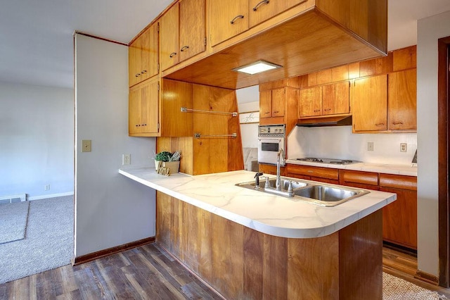 kitchen featuring stovetop, a sink, oven, light countertops, and under cabinet range hood