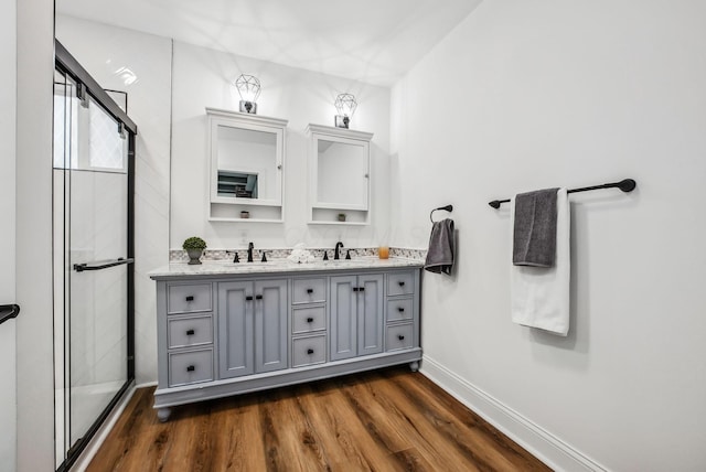 full bath featuring double vanity, a shower stall, wood finished floors, and a sink