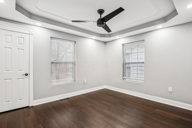 empty room featuring visible vents, baseboards, dark wood finished floors, a raised ceiling, and a ceiling fan