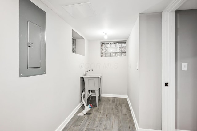 clothes washing area featuring electric panel, baseboards, and wood finished floors