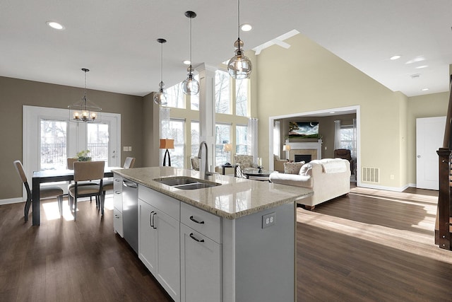 kitchen featuring dark wood-type flooring, a tiled fireplace, an island with sink, light stone counters, and a sink