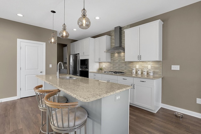 kitchen with a center island with sink, a sink, stainless steel appliances, wall chimney exhaust hood, and backsplash