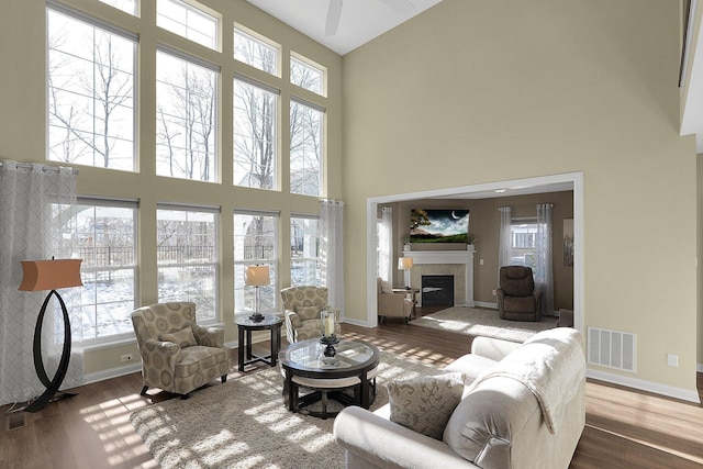 living room with visible vents, baseboards, a high ceiling, wood finished floors, and a glass covered fireplace