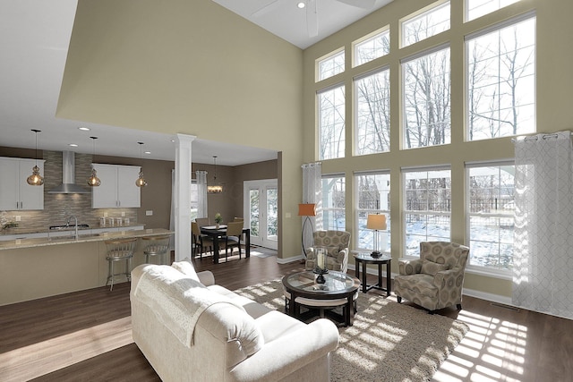 living room featuring dark wood-style floors, visible vents, ornate columns, baseboards, and a high ceiling