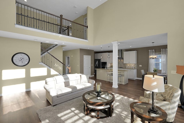 living room featuring baseboards, ornate columns, stairs, dark wood-type flooring, and a notable chandelier