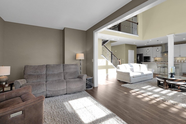 living area with a towering ceiling, stairs, ornate columns, and wood finished floors