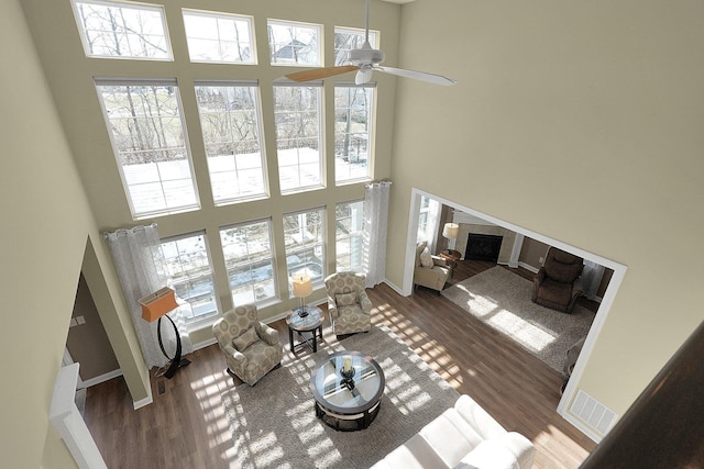 living room featuring visible vents, baseboards, a fireplace, a towering ceiling, and wood finished floors