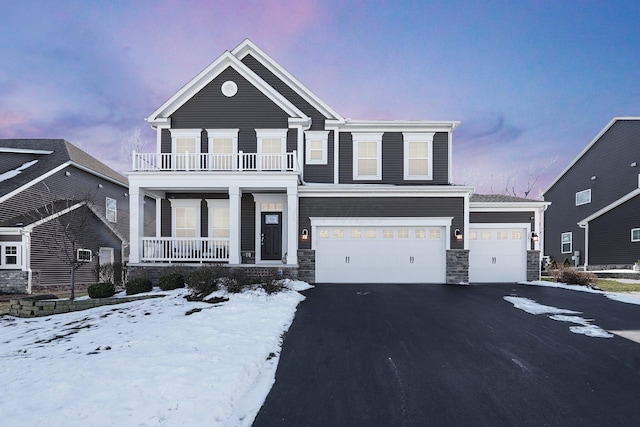 view of front of property featuring a balcony, covered porch, a garage, stone siding, and aphalt driveway