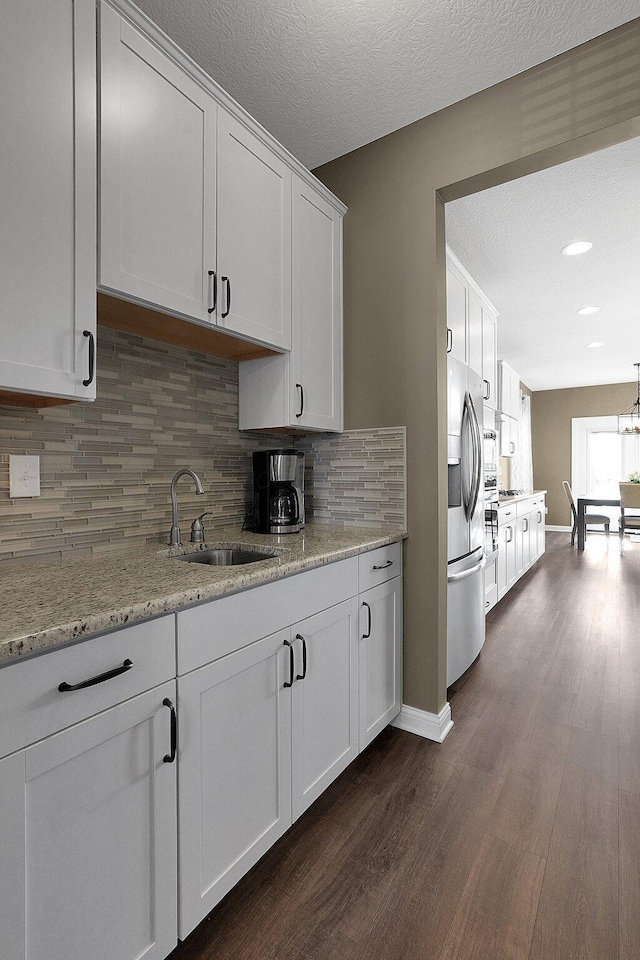 kitchen with stainless steel refrigerator with ice dispenser, a sink, backsplash, dark wood finished floors, and white cabinets