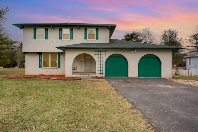 traditional-style home with aphalt driveway, a front yard, covered porch, stucco siding, and a garage