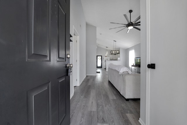 foyer with baseboards, ceiling fan with notable chandelier, dark wood-type flooring, and vaulted ceiling