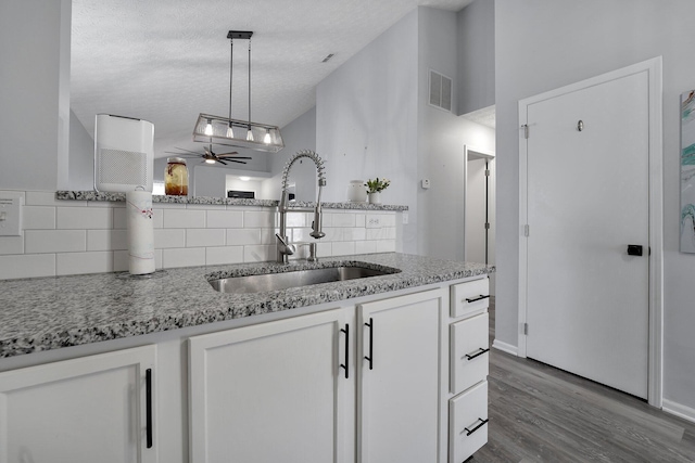 kitchen with visible vents, lofted ceiling, white cabinets, a textured ceiling, and a sink