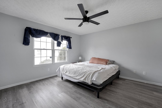 bedroom with a ceiling fan, wood finished floors, baseboards, and a textured ceiling