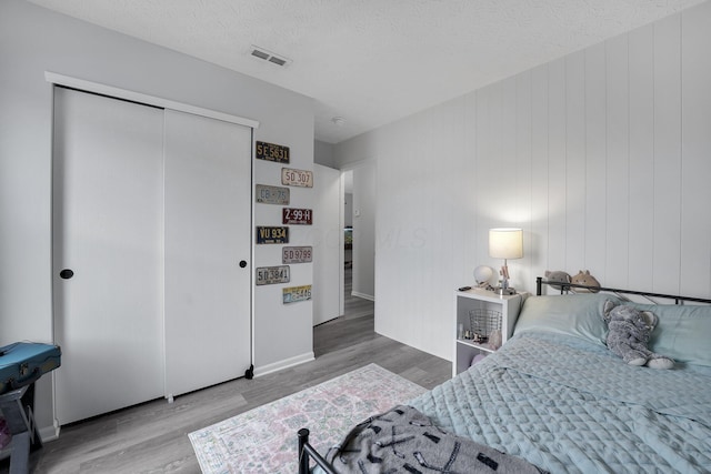 bedroom featuring wood finished floors, visible vents, a closet, and a textured ceiling