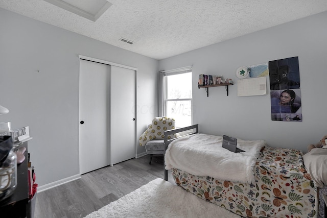 bedroom with visible vents, a textured ceiling, wood finished floors, a closet, and baseboards